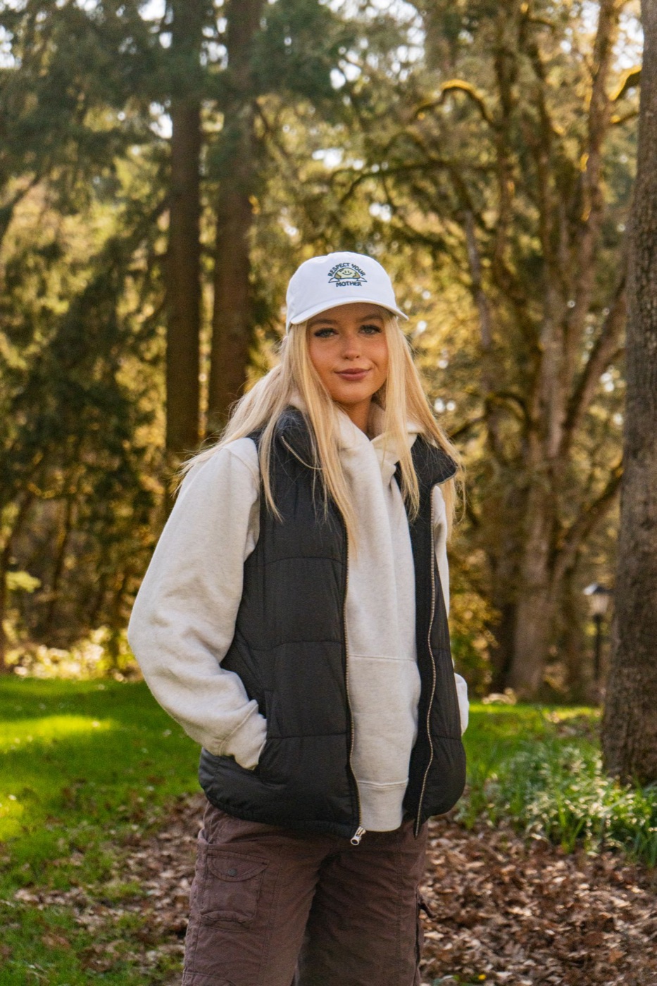 Model in a white Respect Your Mother cap and puffer vest in the forest