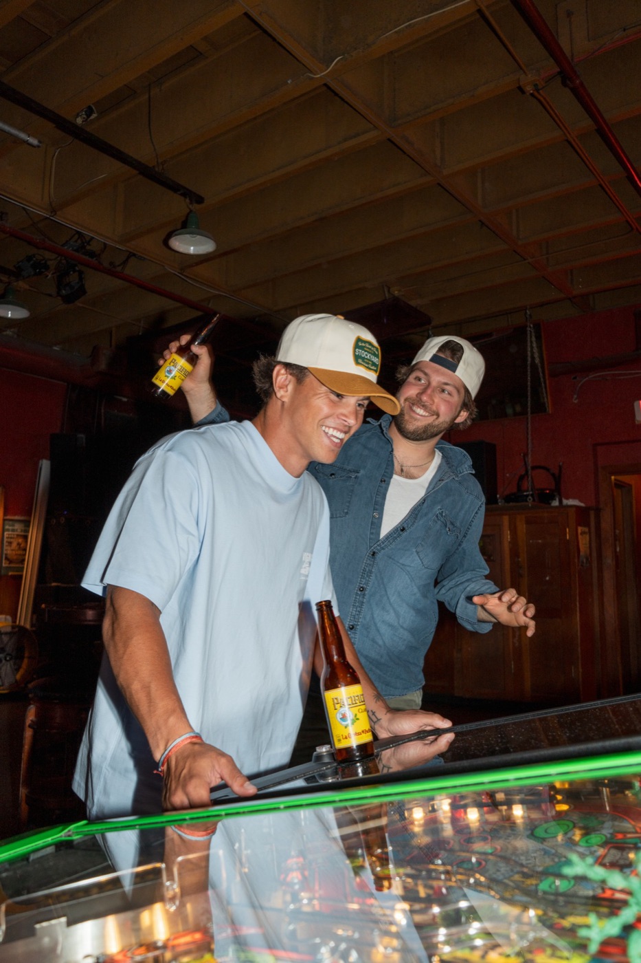 Two friends in Stockyard caps playing pinball