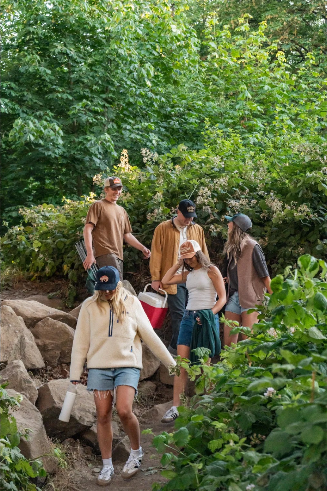 Five friends in trucker caps walking down a rocky trail to the river