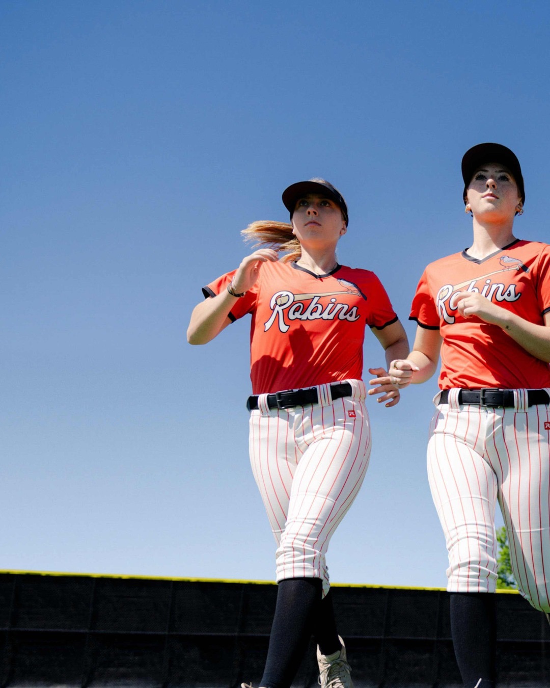 Two softball players in red jerseys jogging